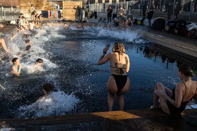 Un grupo de personas saltando a una piscina de agua fría y salpicando agua por todas partes.