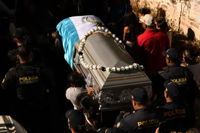 Un grupo de policías, de espaldas, cargan un féretro cubierto con la bandera de Guatemala.