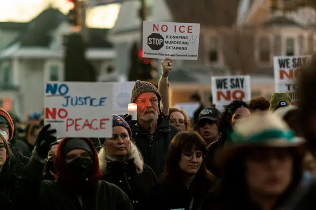 Varios participantes sostienen en alto carteles en los que se lee "No Justicia, no paz", "No ICE", durante vigilia multitudinaria por la muerte a tiros de Renee Nicole Goods a manos de un agente federal durante una redada migratoria en Mineápolis, Minesota, Estados Unidos, el 7 de enero de 2025. (Foto de Kerem YUCEL / AFP vía Getty Images)