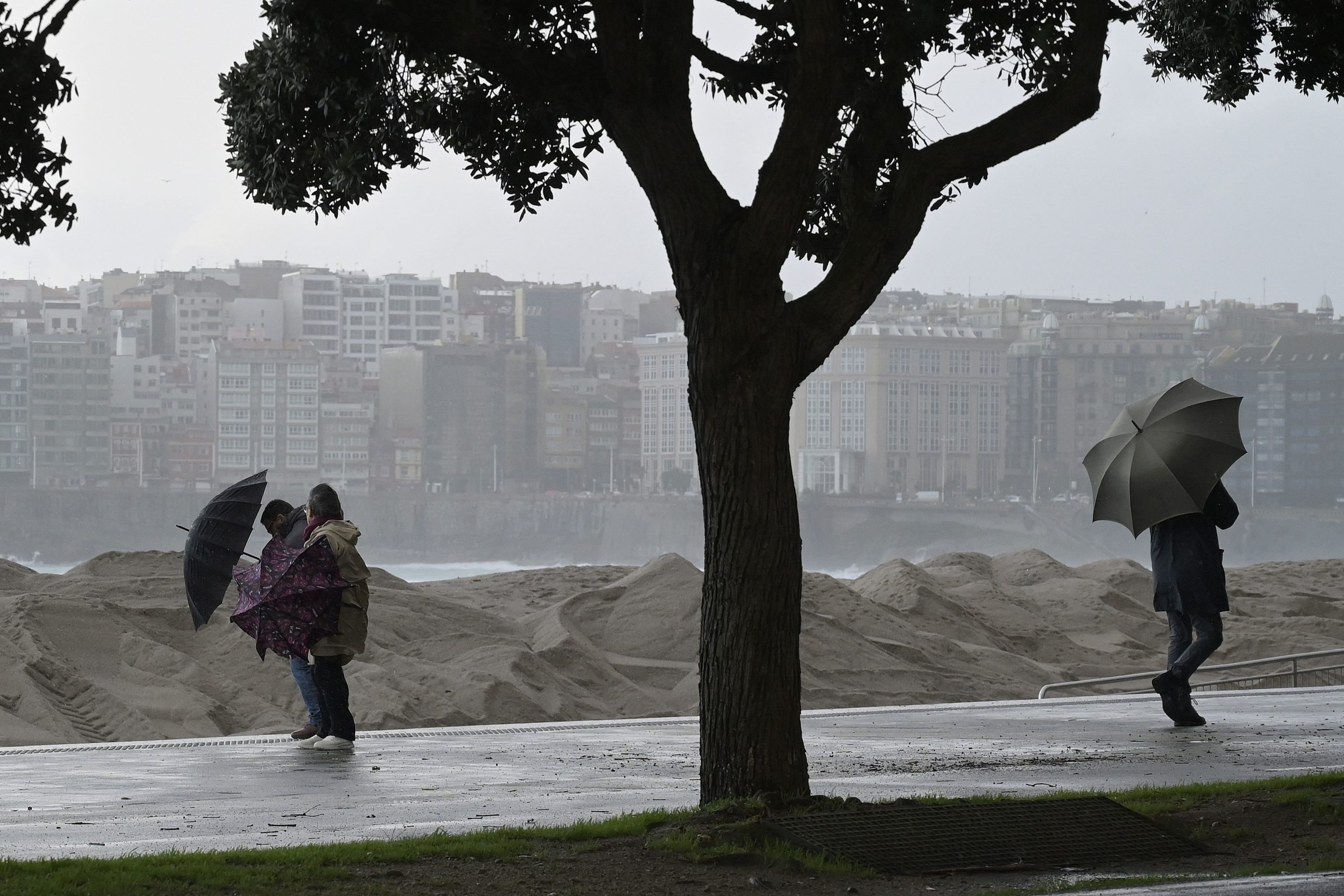 Varias personas se protegen de la lluvia junto a la costa de A Coruña.