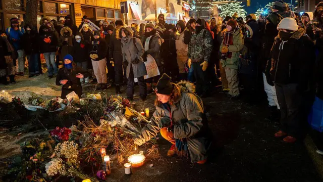 Personas colocan arreglos florales en el suelo, así como velas, para honrar la memoria de alex pretti.