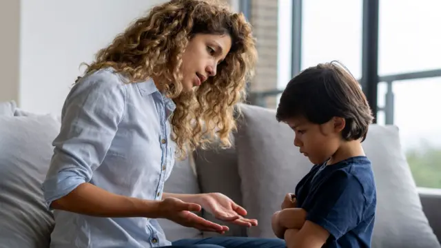 Un niño, cabizbajo y con los brazos cruzados, rehúsa a negociar con su madre que intenta calmadamente razonar con él