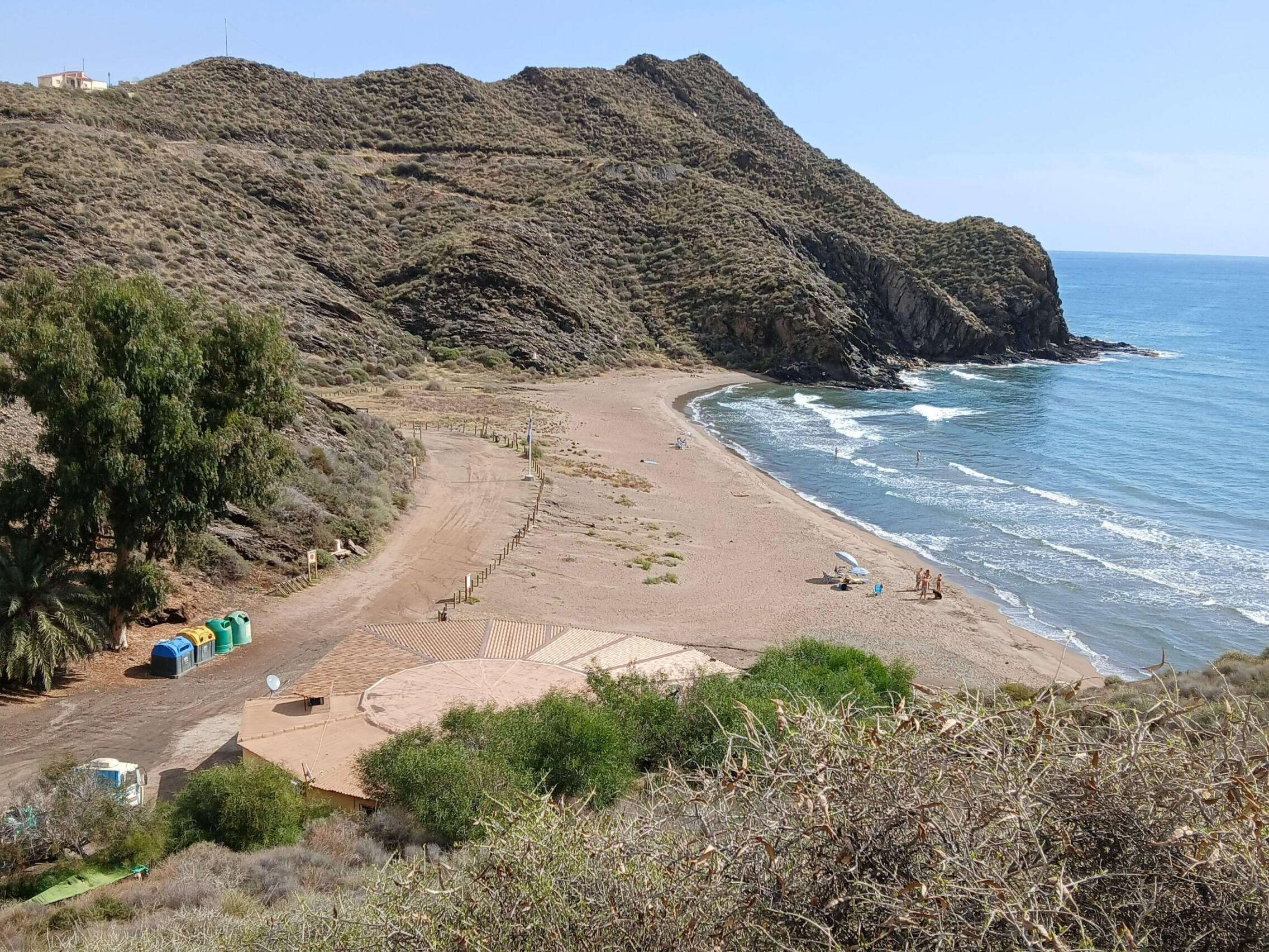 Foto: Cala de aguas limpias y arena oscura encajada entre lomas áridas y acantilados del litoral lorquino. (Extraída de X)
