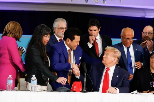 Trump saluda a la gente que se acerca a la mesa donde está sentado