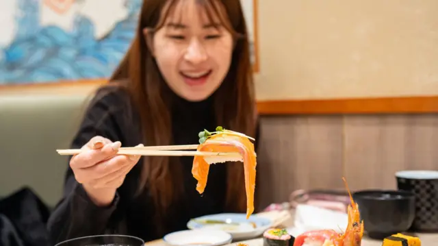 Un primer plano de una joven asiática feliz en un restaurante japonés, a punto de comer un nigiri de salmón.