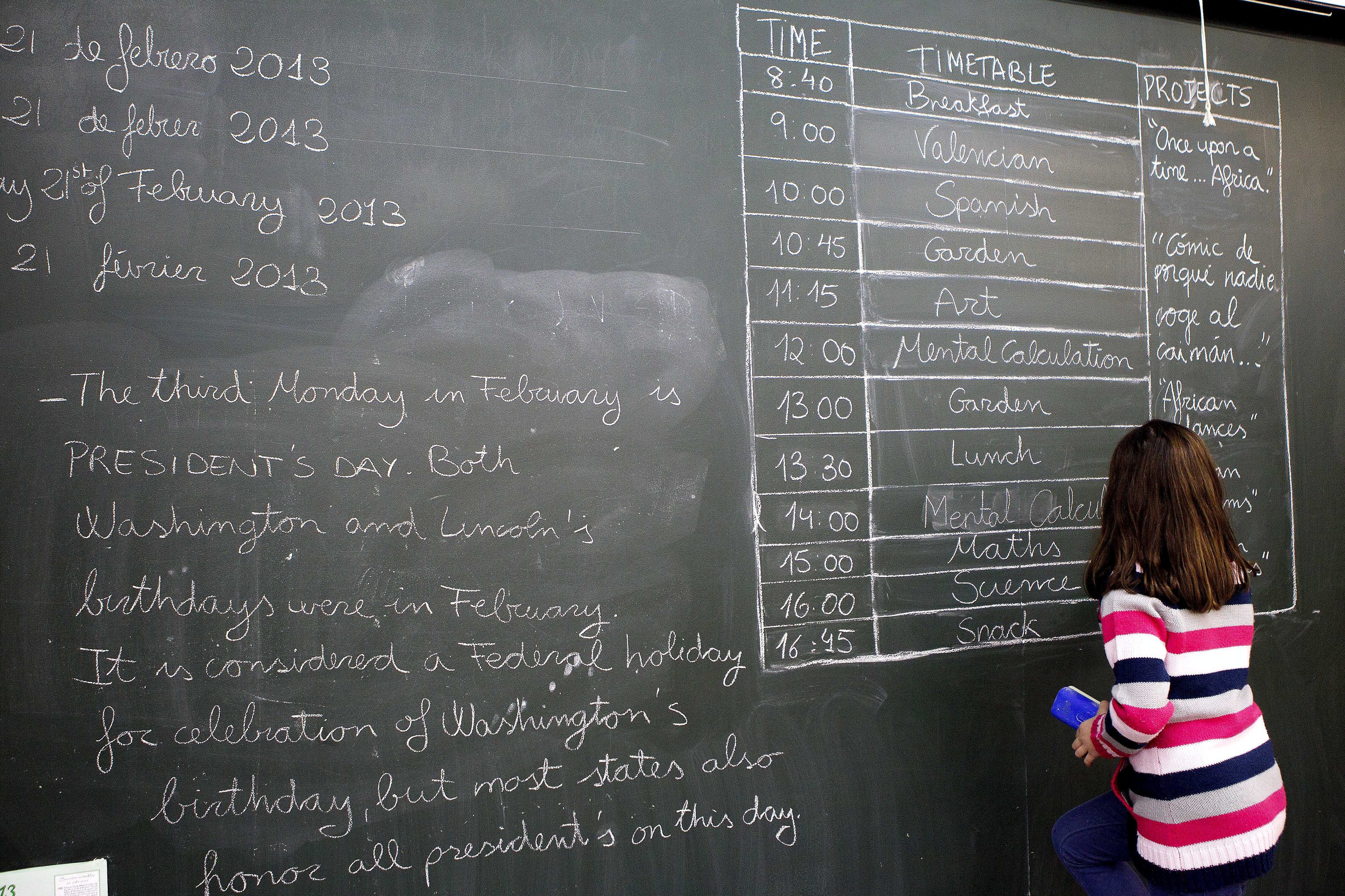 Una alumna de Valencia escribe el horario en inglés en la pizarra del aula.