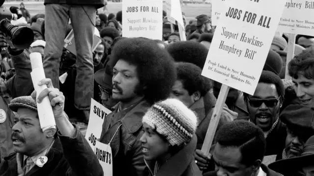 Una foto en blanco y negro de un joven Jesse Jackson participando en una marcha por el empleo.