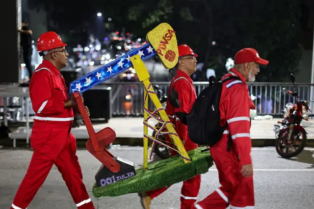 Unos trabajadores de Pdvsa cargan una maqueta de un balacín de petróleo.