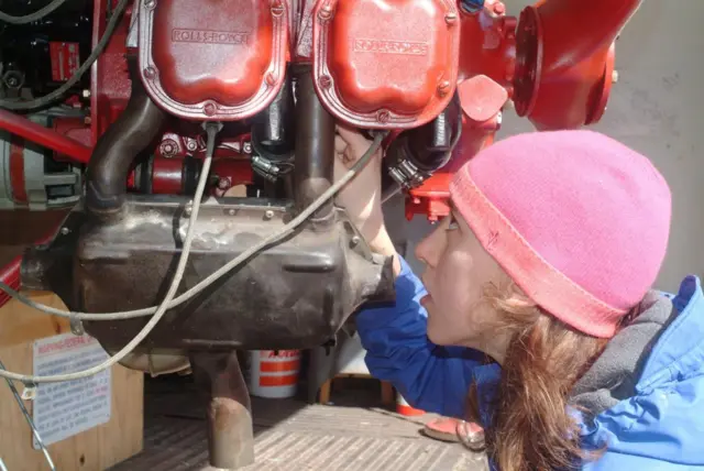 Sabrina González Pasterski, con un gorro rosado y una chaqueta azul, trabajando en unas piezas de color naranja del avión
