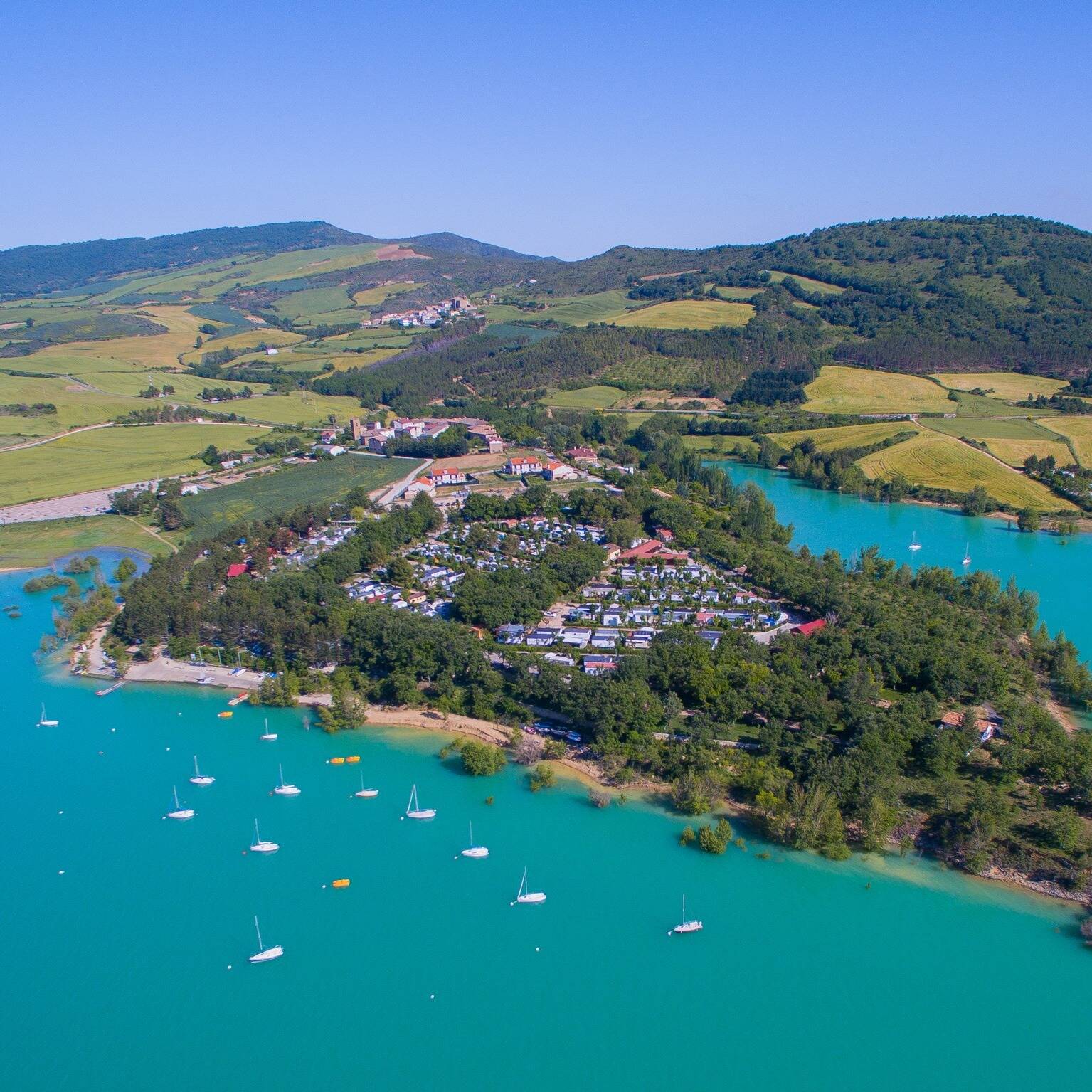 Foto: Vista aérea del camping ubicado junto al embalse de Alloz, en Navarra, rodeado de colinas verdes y aguas turquesas. (Extraída de Facebook)