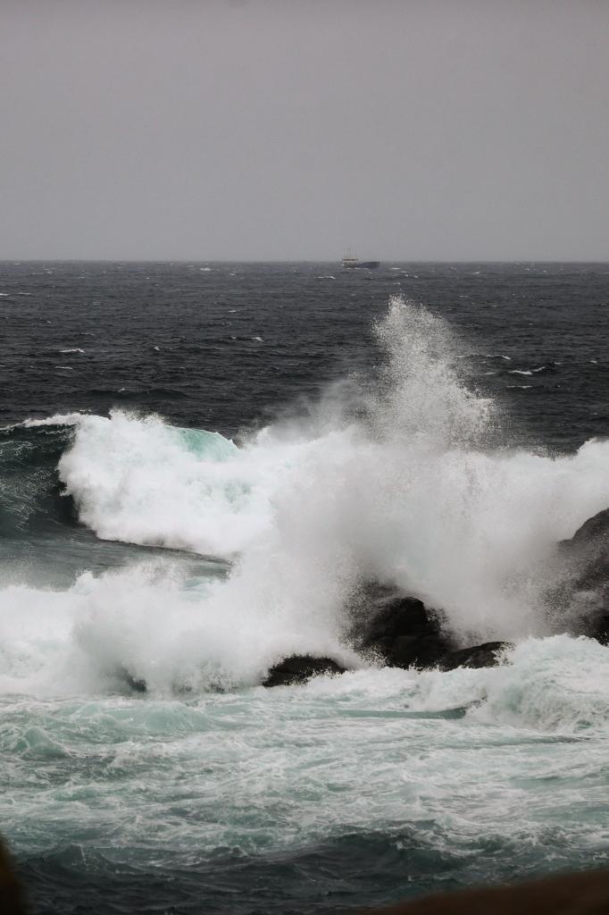 Una ola rompe contra las rocas de A Coruña mientras el buque 'Anmare' se dirige a puerto,