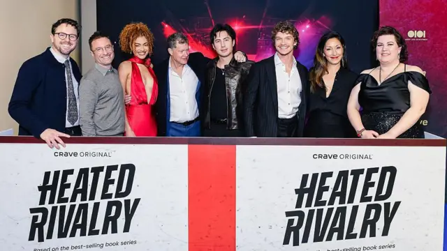 Brendan Brady, Jacob Tierney, Ksenia Daniela Kharlamova, Dylan Walsh, Hudson Williams, Connor Storrie, Christina Chang y Rachel Reid detrás de una valla publicitaria de Heated Rivalry en el estreno de Toronto.