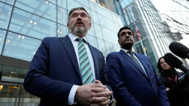 Ro Khanna y Thomas Massie están frente a un edificio de vidrio mientras varios micrófonos apuntan hacia ellos.