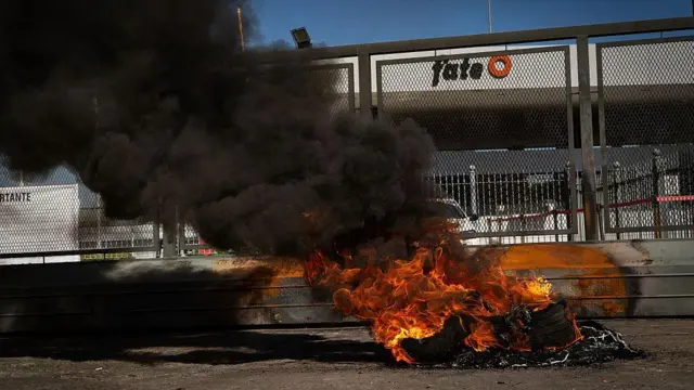 Columnas de humo negro se elevan desde neumáticos incendiados en protesta frente a las puertas cerradas de FATE, el 18 de febrero de 2026. 