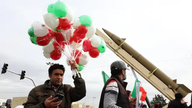 Un hombre iraní sostiene un manojo de globos verdes, rojos y blancos cerca de un misil balístico durante las celebraciones que marcan el 47.º aniversario de la revolución islámica en Teherán, Irán (11 de febrero de 2026).