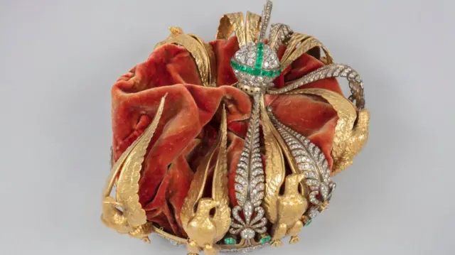La corona de la emperatriz francesa Eugenia: una corona de oro con diamantes, esmeraldas y águilas doradas, cubierta de terciopelo rojo. Sus decoraciones se pueden ver aplastadas hacia dentro.