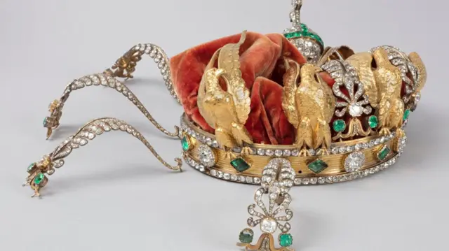 La corona de la emperatriz francesa Eugenia: una corona de oro con diamantes, esmeraldas y águilas doradas, cubierta de terciopelo rojo. Sus decoraciones se pueden ver aplastadas hacia dentro.