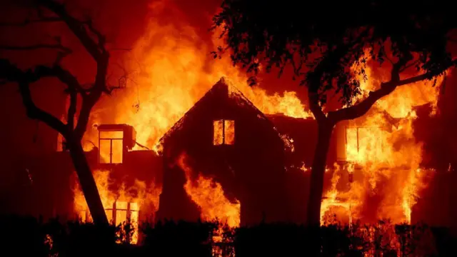 Una imagen nocturna de una casa en llamas, azotada por fuertes vientos, en Los Ángeles durante los incendios de enero de 2025.