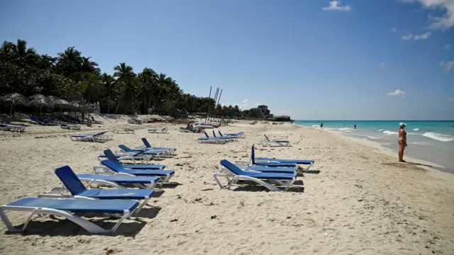 Una fila de tumbonas azules vacías se extiende sobre la arena blanca de una playa en la península de Varadero, en Cuba.