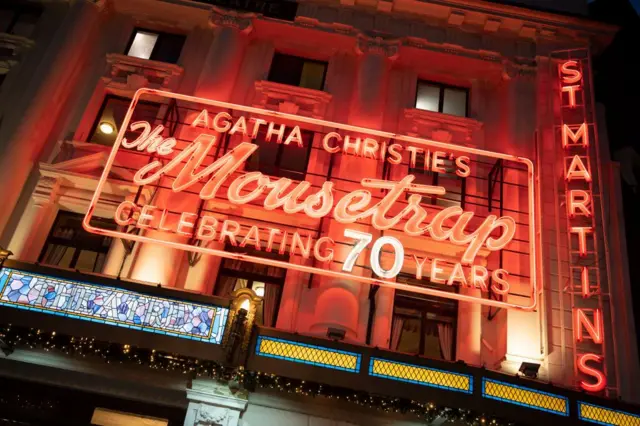Exterior nocturno del anuncio luminoso del teatro que dice "La Ratonera, celebrando 70 años".