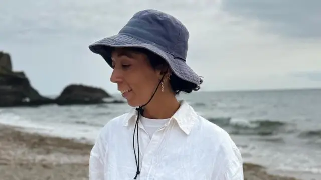 Una mujer con cabello castaño rizado que lleva una gorra azul oscuro y una camisa blanca.