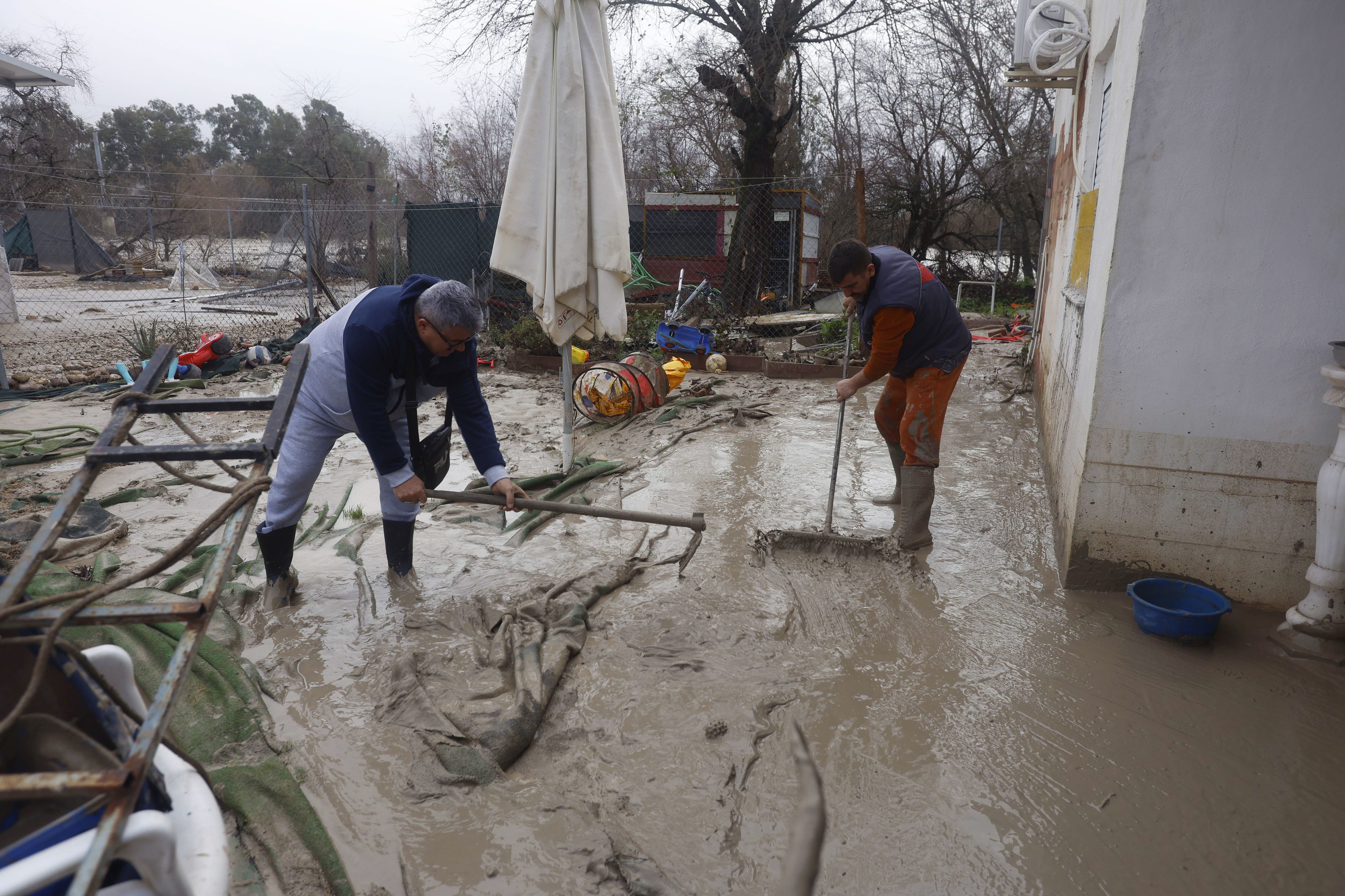 Vecinos de las parcelas próximas al río Guadalquivir en Córdoba limpian el lodo acumulado al regresar a sus viviendas.