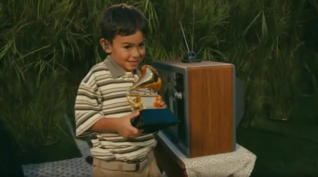 Un niño con un Grammy en las manos junto a un televisor en el que se ve el momento en que Bad Bunny recibió el premio.