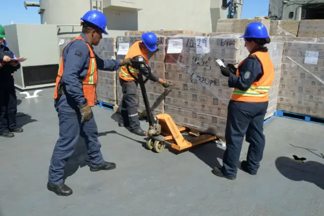 Tres personas supervisan el cargamento de alimentos de un buque naval mexicano