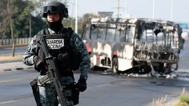Un miembro de la Guardia Nacional monta guardia cerca de un autobús incendiado por grupos del crimen organizado en respuesta a un operativo en Jalisco para detener a un objetivo de seguridad prioritario,