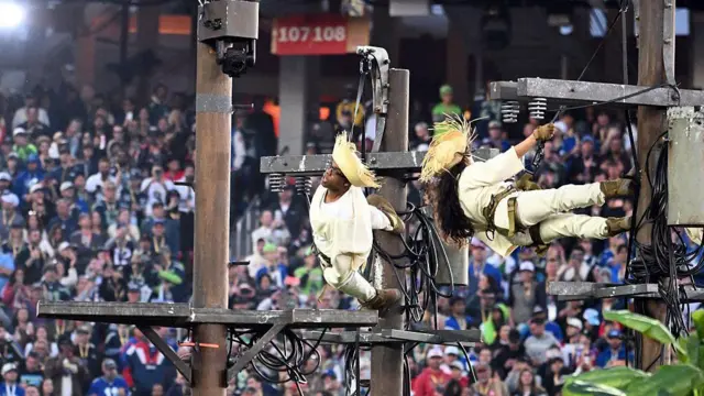 dos bailarínes cuelgan de postes eléctricos que simulan la infraestructura de la isla en el show de medio tiempo de bad bunny en el superbowl.