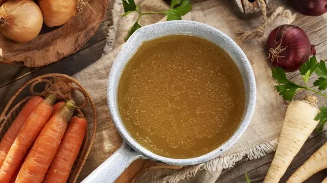 Caldo o sopa de huesos de pollo en una cacerola con verduras frescas sobre una mesa de madera