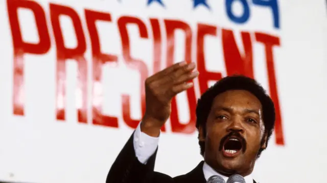 Jesse Jackson haciendo campaña en 1984 frente a un gran cartel que dice "presidente".
