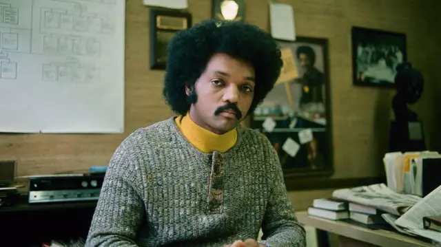 Jesse Jackson en los inicios de su carrera. Está sentado en una oficina mirando directamente a la cámara.