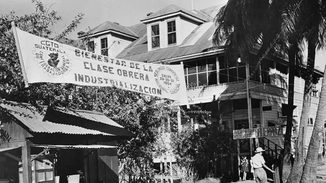 Una fotografía en blanco y negro muestra la sala de contratación de la United Fruit Company en Puerto Barrios, el mayor puerto guatemalteco del Caribe. La bandera de la Confederación General de Trabajadores, el principal sindicato de Guatemala, cuelga del edificio.