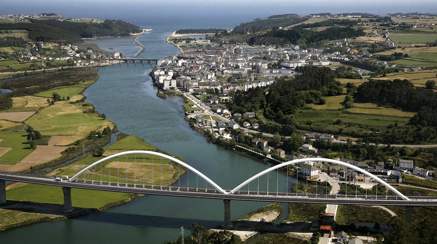 Foto: Panorámica del pueblo, con su casco urbano extendiéndose junto a la ría y el puente que vertebra la entrada a la villa. (Extraída de Facebook)