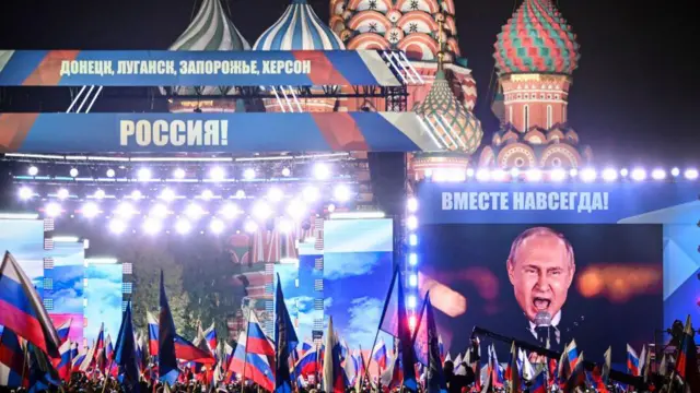 El presidente ruso, Vladímir Putin, visto en una pantalla gigante mientras se dirige a una multitud de seguidores en un mitin-concierto en la Plaza Roja de Moscú en 2022. Hay muchas banderas de Rusia entre el público.