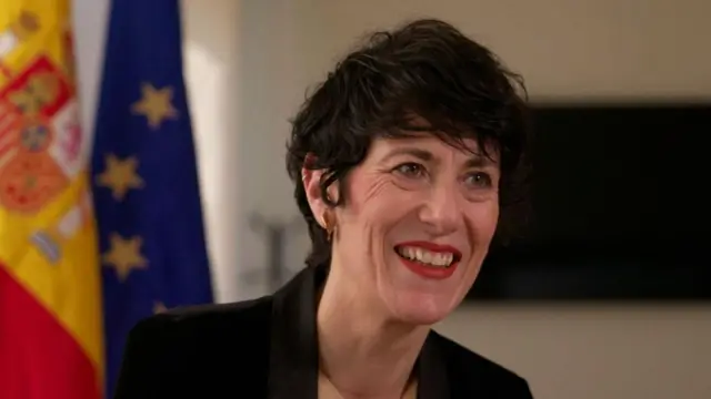 Elma Saiz, ministra de Inclusión, Seguridad Social e Inmigración, sonríe ante las banderas de España y la UE
