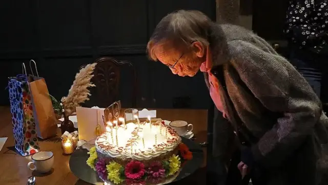 Margaret Bradshaw sopla las velitas en una gran torta de cumpleaños cubierta de crema y decolorada con flores