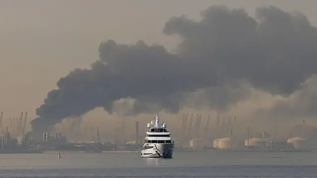 Un yate navega frente a una columna de humo que se eleva desde el puerto de Jebel Ali, tras un presunto ataque iraní en Dubái el 1 de marzo de 2026.