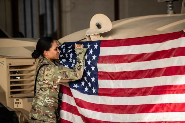 Una soldado estadounidense coloca una bandera de su país en un vehículo militar en Siria.