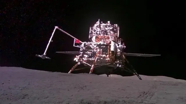 En la imagen aparece el módulo lunar chino de aterrizaje y ascenso, captado por la "cámara móvil" que lleva la sonda Chang'e-6 (fuera de cuadro), mientras sostiene una bandera china sobre la superficie lunar, con el oscuro abismo del espacio como telón de fondo, durante la misión lunar de China el 4 de junio de 2024.