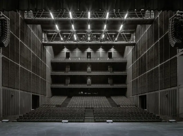 Auditorio amplio visto desde el escenario, con varias balconadas, paredes acústicas oscuras y un techo iluminado con estructura metálica.