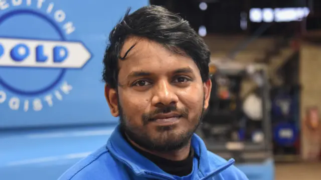 Ajay Kumar Chandapaka, frente a un camión azul, con una chaqueta del mismo color 