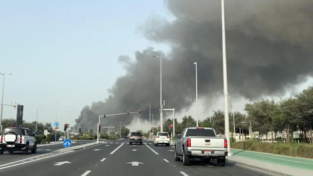 Varios vehículos en una carretera de varios carriles en Abu Dhabi con columnas de humo que se ven a lo lejos