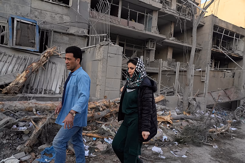People walk past buildings damaged during a strike on a police station during ongoing, joint U.S.-Israeli military attacks in Tehran, Iran, 2 March 2026.
