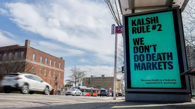 Un cartel de Kalshi en el que dice que la regla número 2 de Kalshi es no participar en mercados de predicción de muertes. A lado circulan autos. Foto tomada en Washington DC