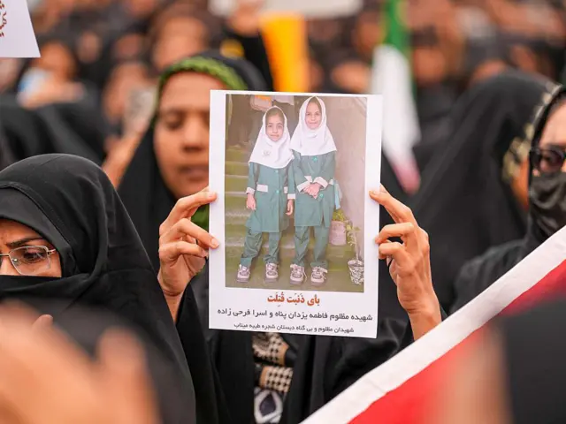 Mujeres sostienen una foto de dos niñas en el funeral en Minab
