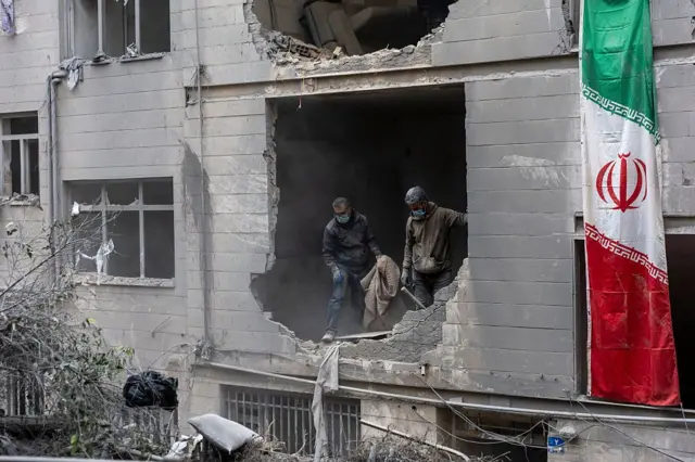Dos personas se asoman a un agujero en un edificio alcanzado por un misil en Irán.