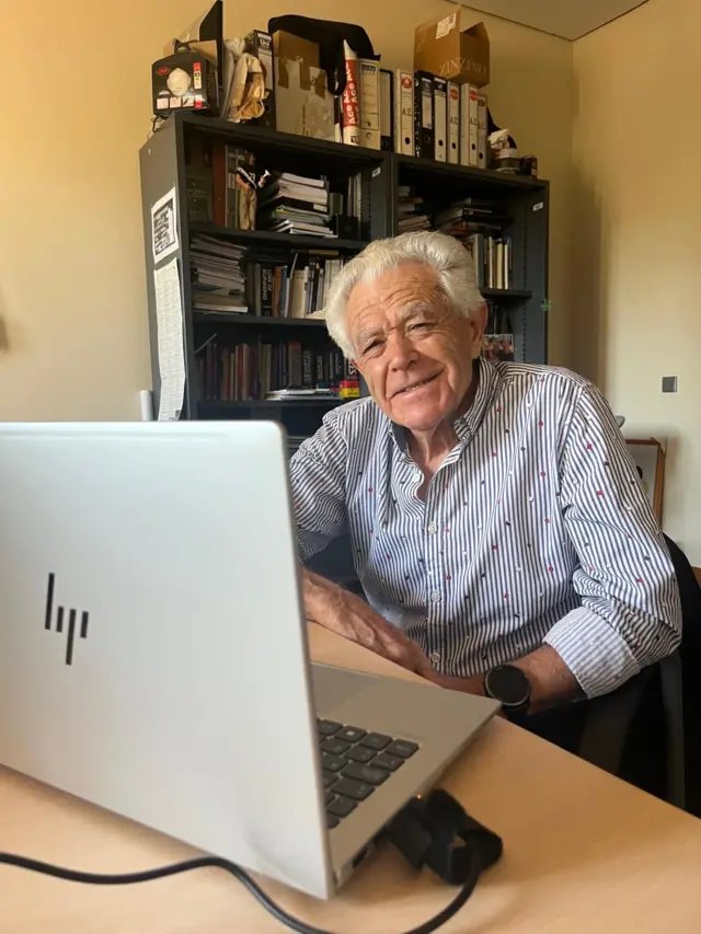 Juan López González mira sonriente a la cámara, desde detrás de portátil