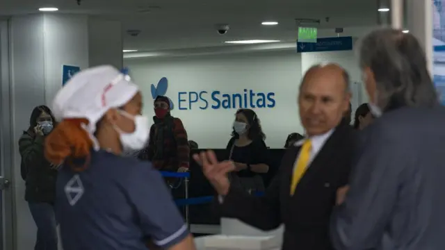 El interior de un edificio de una EPS muestra trabajadores, pacientes y un letrero en el que se lee EPS Sanitas